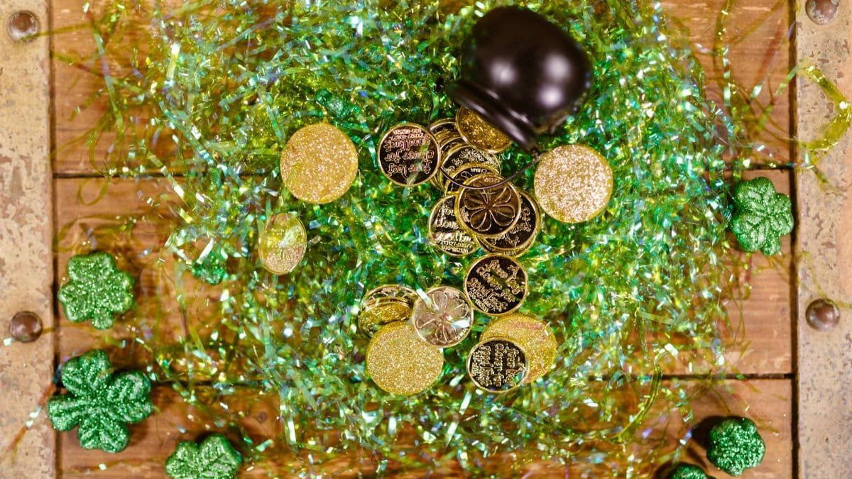 Overhead view of gold coins and shamrocks celebrating St. Patrick's Day with festive green tinsel.