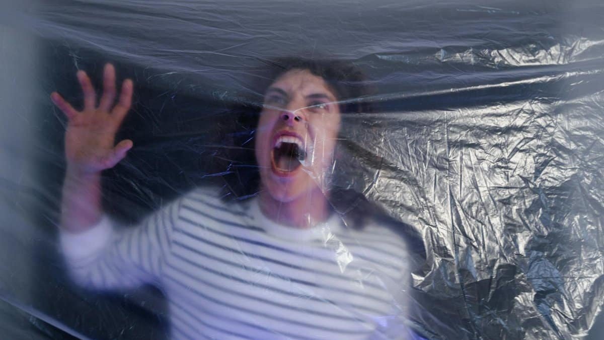 Man in striped shirt screaming behind translucent plastic foil, conveying fear.