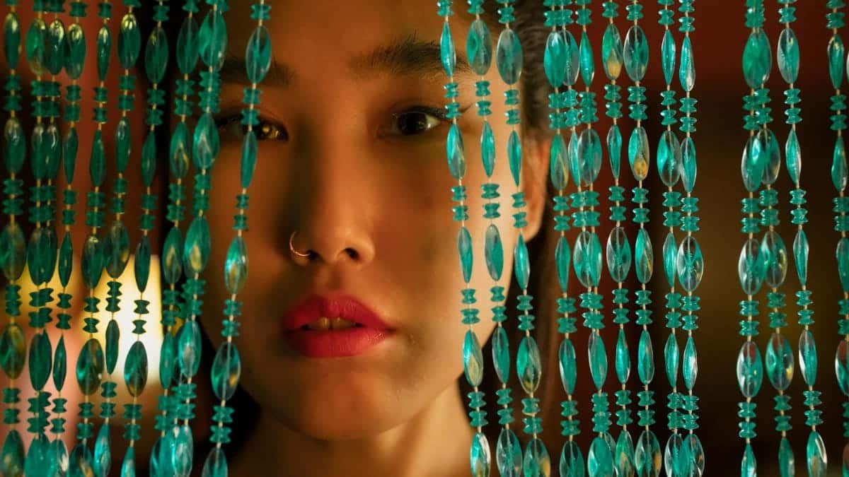 Close-up portrait of a woman behind an intricate turquoise beaded curtain.