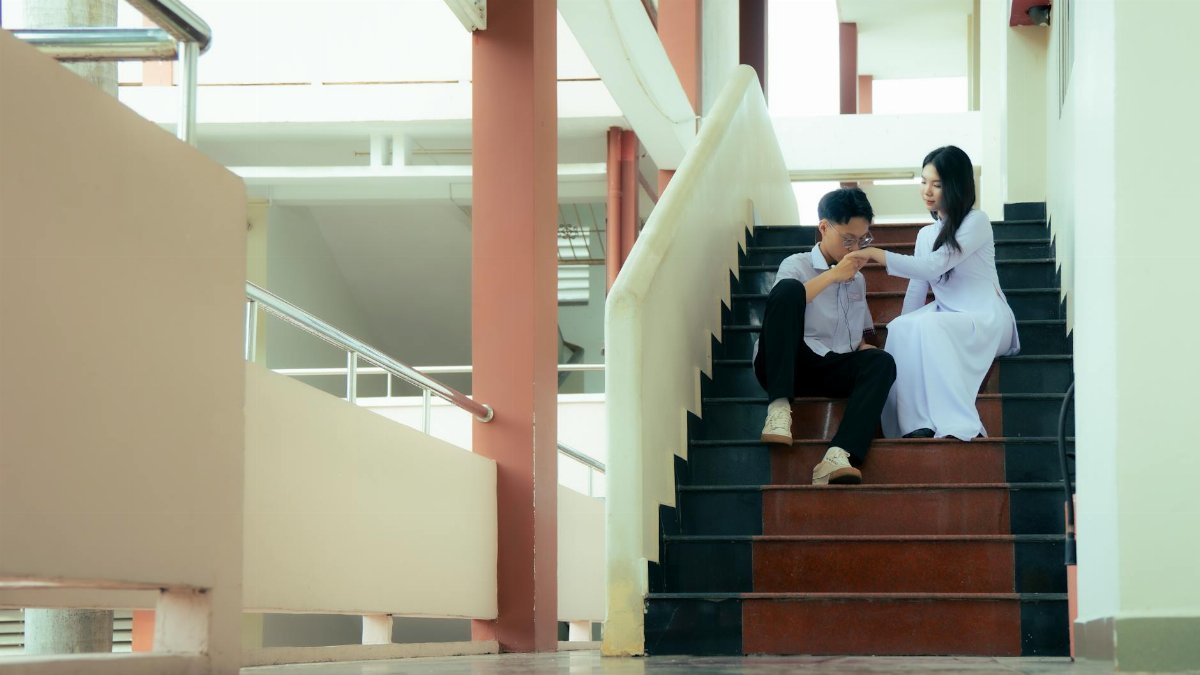 A young couple sitting on school stairs sharing an intimate moment indoors.
