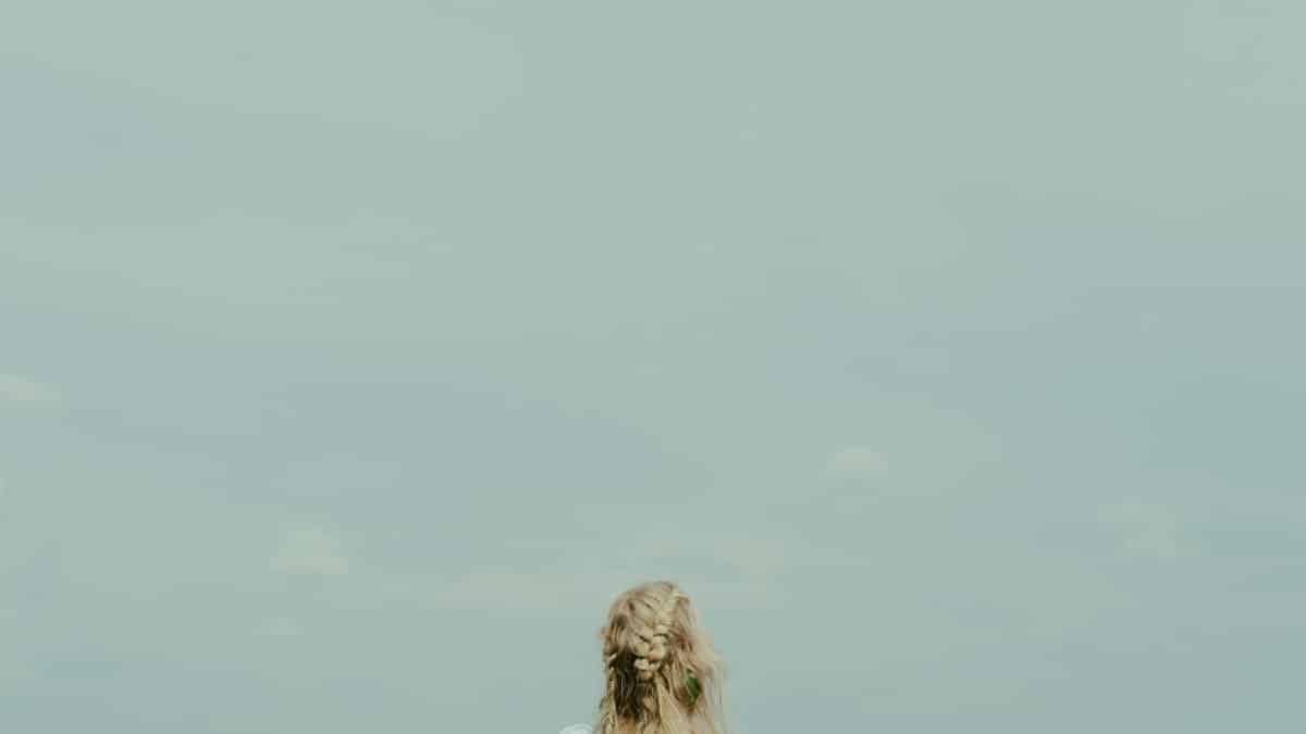 A woman with blonde hair stands outdoors, gazing at an expansive blue sky, embodying freedom and tranquility.
