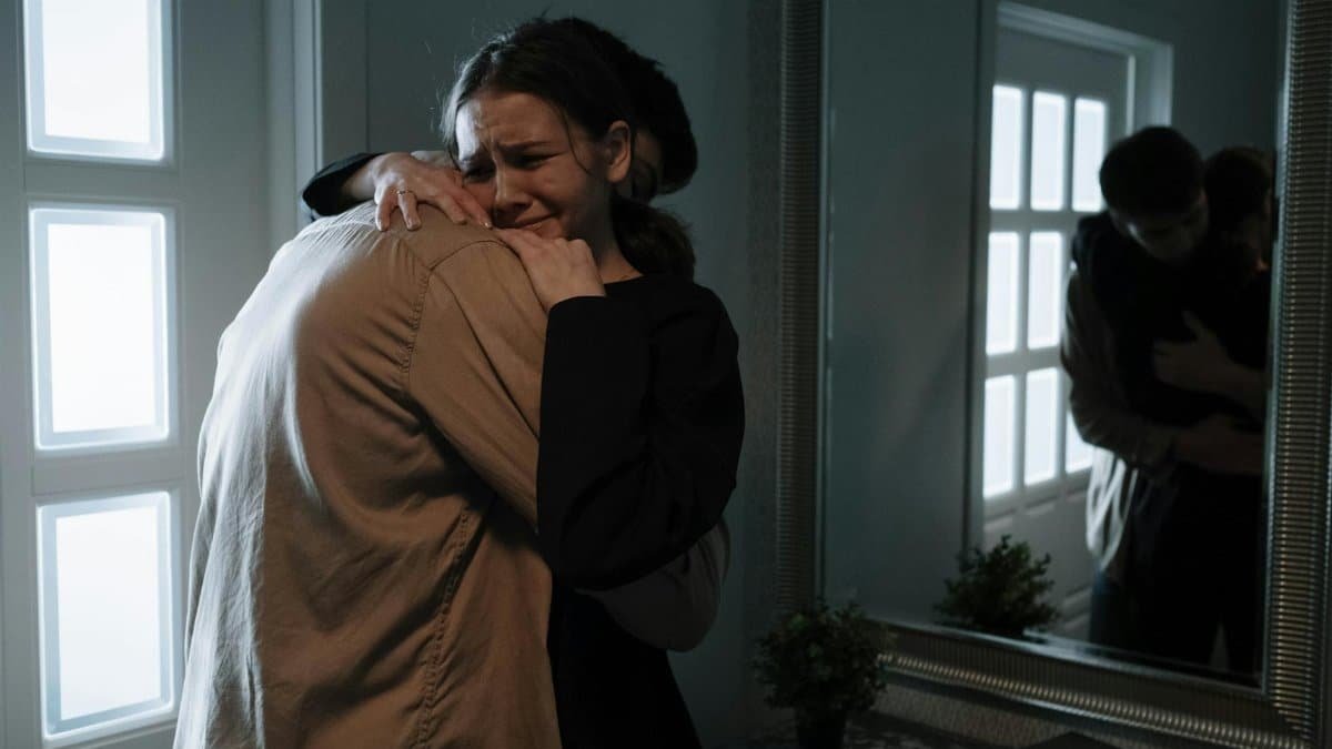 A touching scene of two adults hugging with reflection in mirror, indicating emotional support.