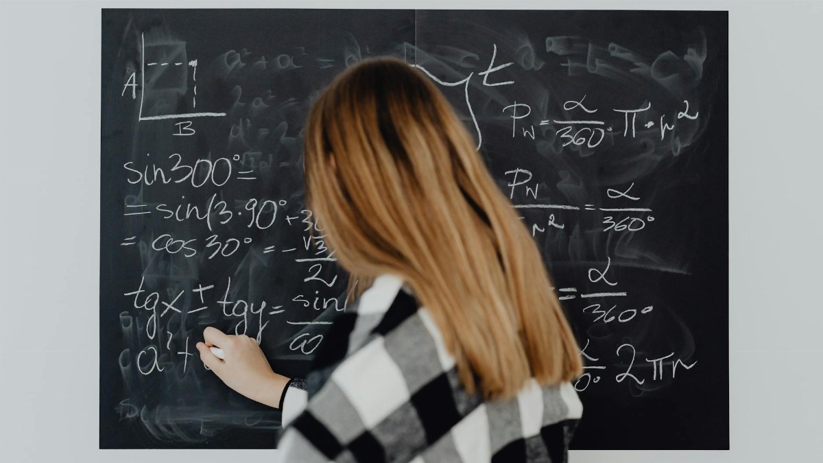 A woman writing mathematical equations on a blackboard, illustrating education and learning.