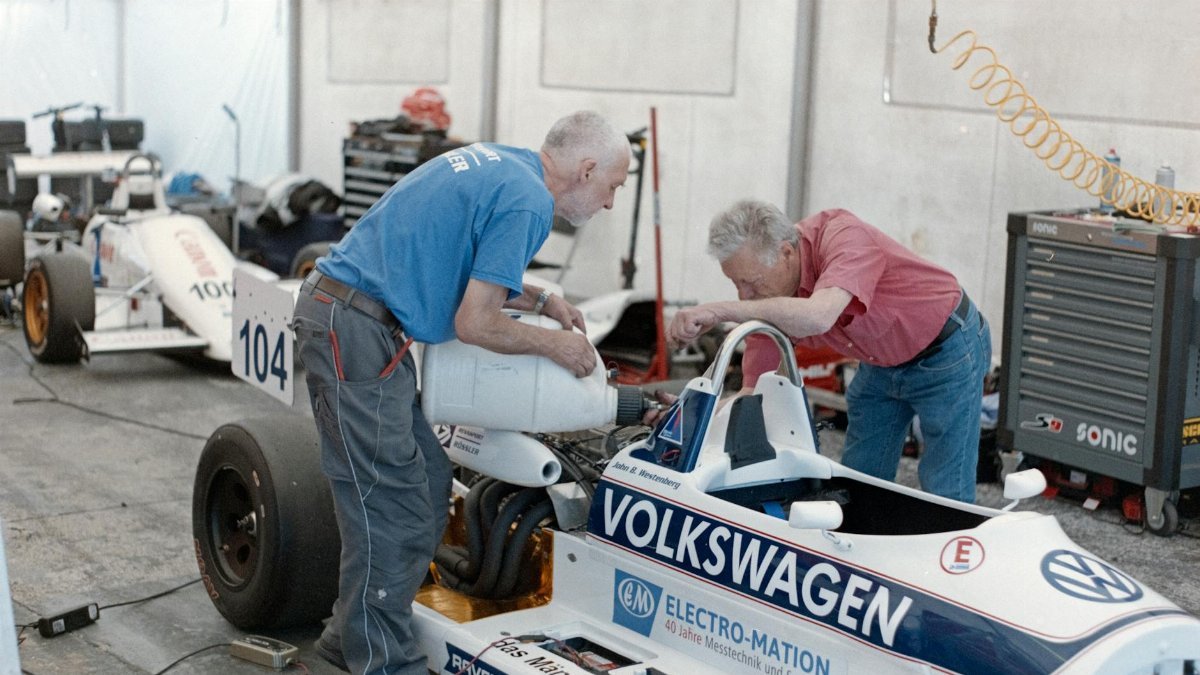 Two senior mechanics servicing race cars in a workshop garage.