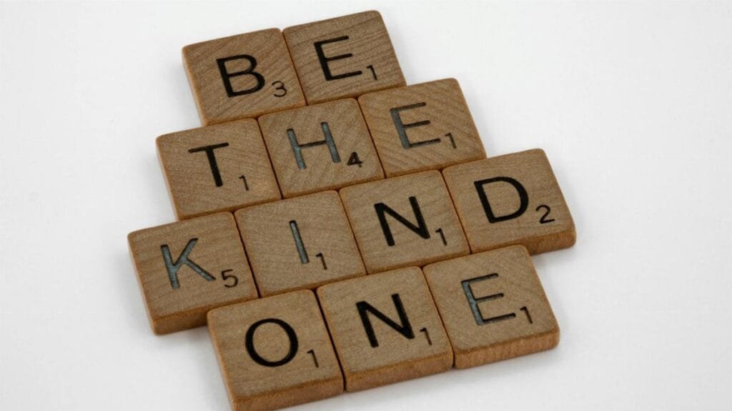 Close-up of wooden letter tiles forming the message 'Be the kind one' on a white surface.