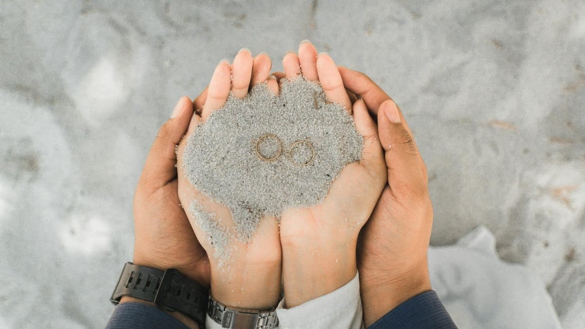 Close-up of a couple holding wedding rings in sand, symbolizing love and union.