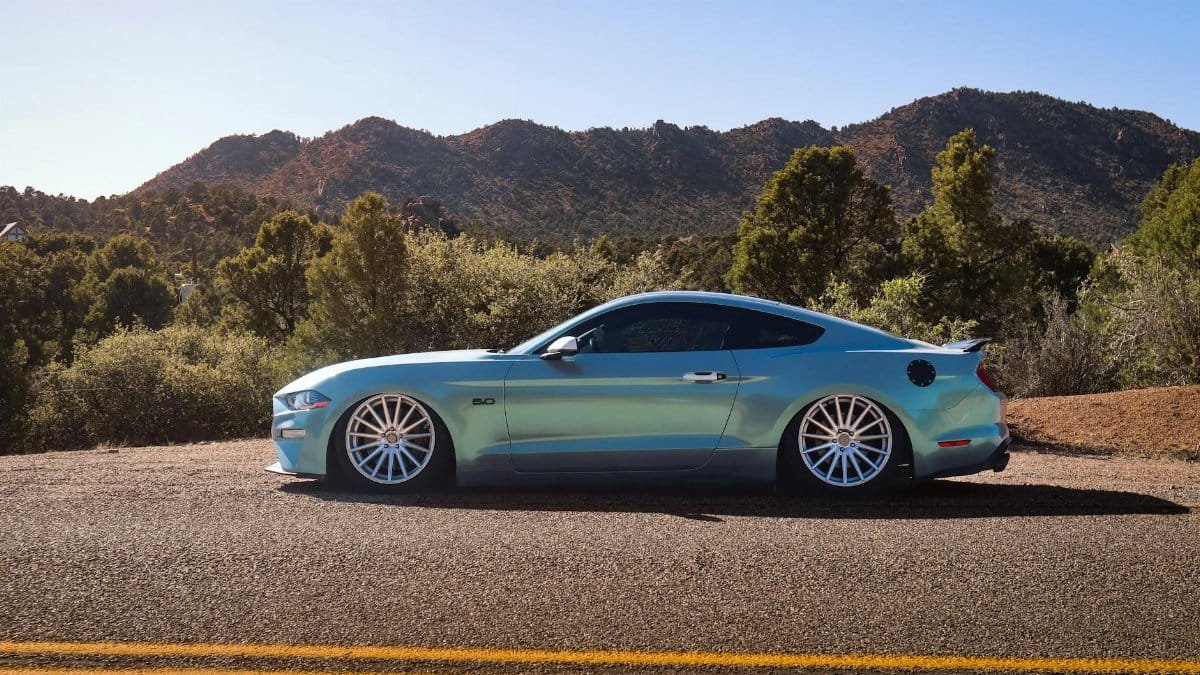 Blue sports car parked on a mountain road under clear skies, scenic drive.