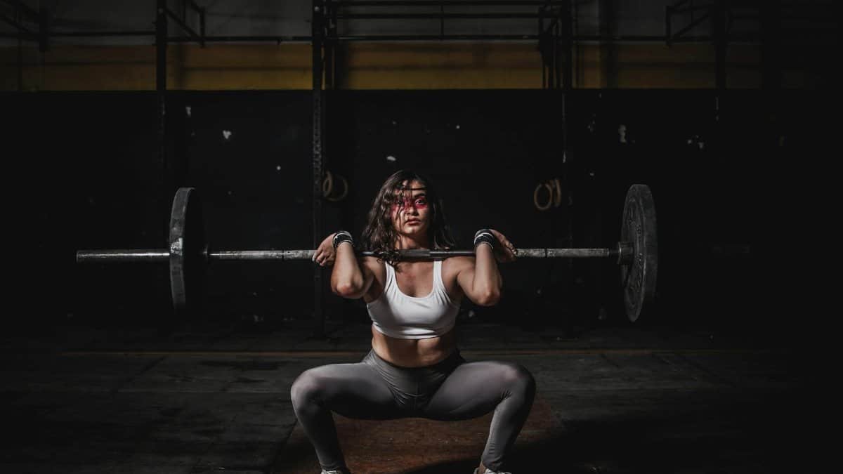 A strong female weightlifter squats with a barbell in a dimly lit gym, showcasing power and fitness.