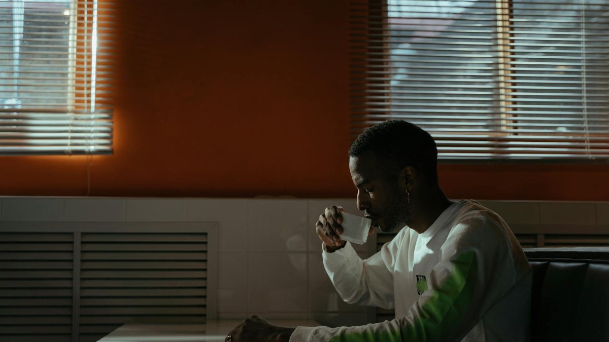 A man seated in a café, enjoying a cup of coffee with sunlight streaming through the windows.