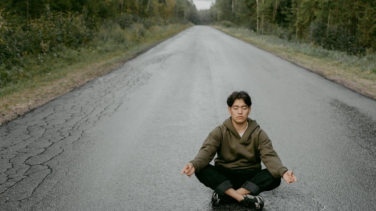 A man practices meditation in a yoga pose on a quiet forest road, emphasizing mindfulness and well-being.