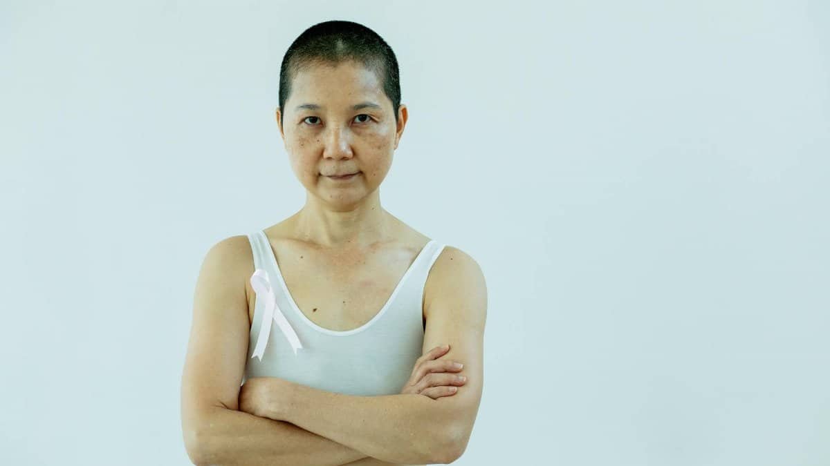 Asian woman with short hair wearing a pink ribbon, representing breast cancer awareness and resilience.