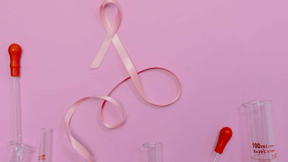 Pink ribbon symbolizing breast cancer awareness with laboratory glassware on a pink backdrop.