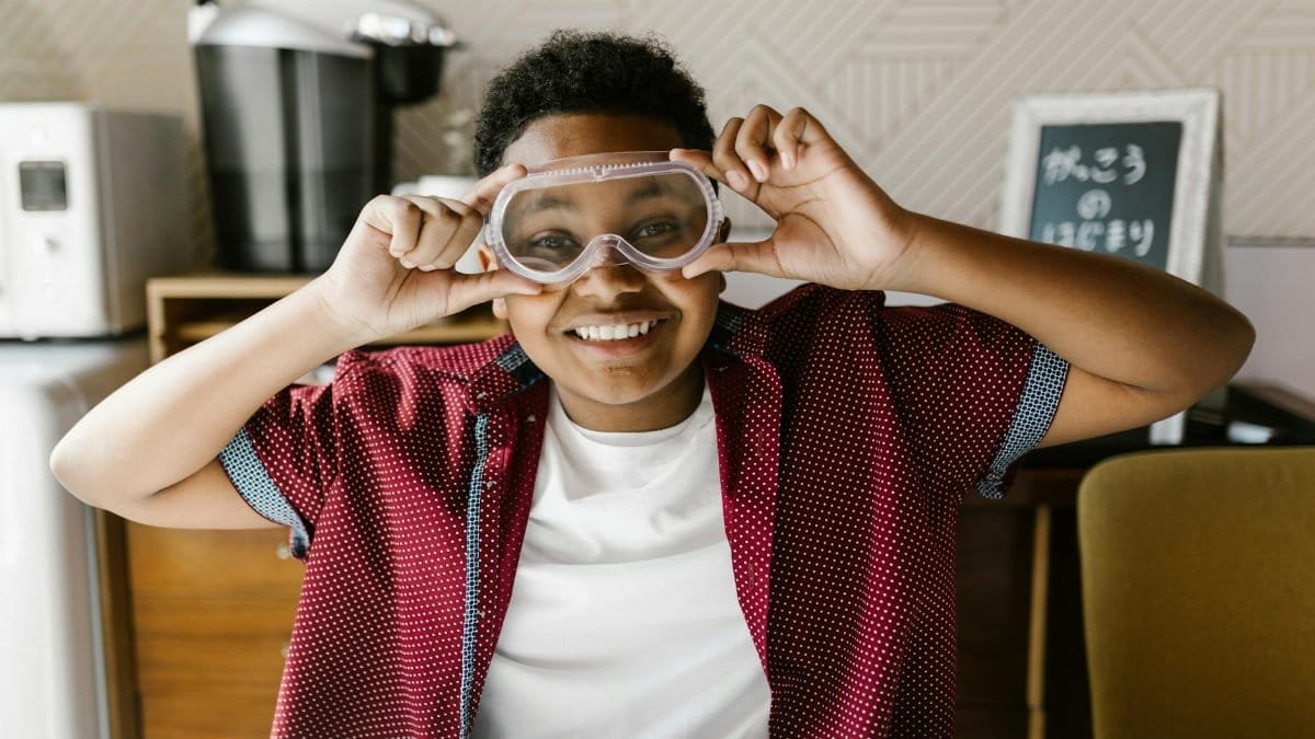 A cheerful boy wearing goggles indoors, partaking in a school project.