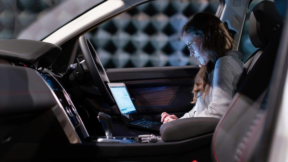 Woman working on a laptop inside a car, testing sound engineering in an isolated chamber.