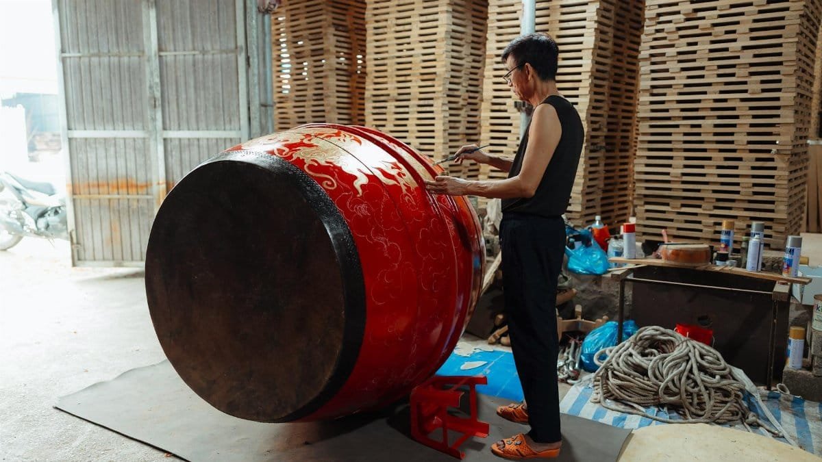 A craftsman working on a large red traditional Asian drum in a workshop, showcasing cultural craftsmanship.