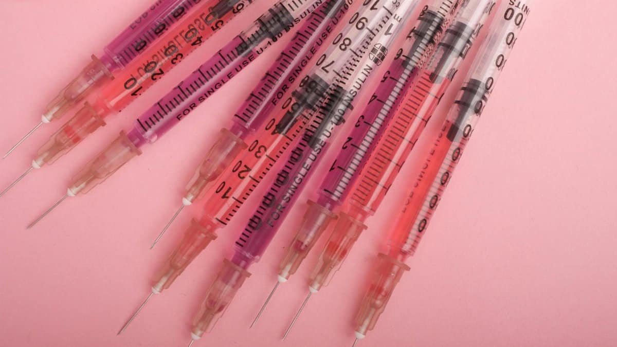 Vibrant syringes arranged on a pink backdrop, highlighting medical tools.