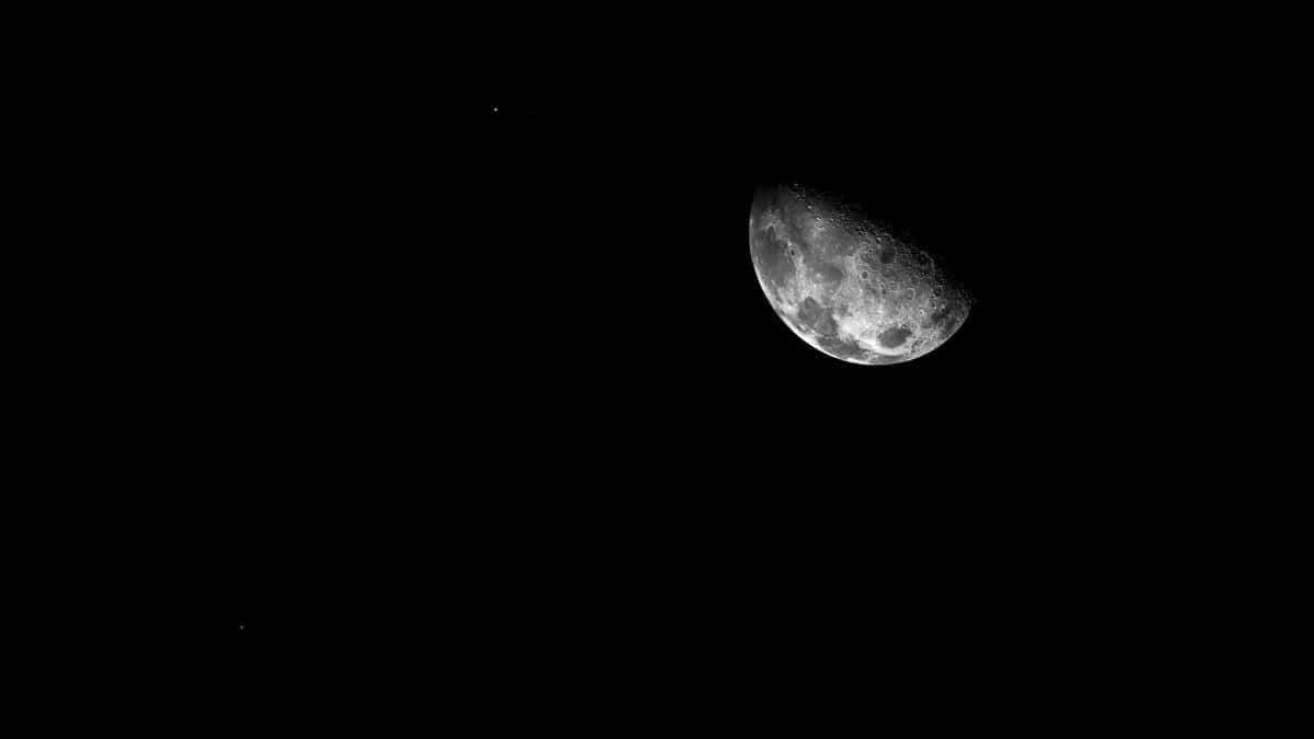 From below third quarter glowing moon shining on dark starless sky at late night