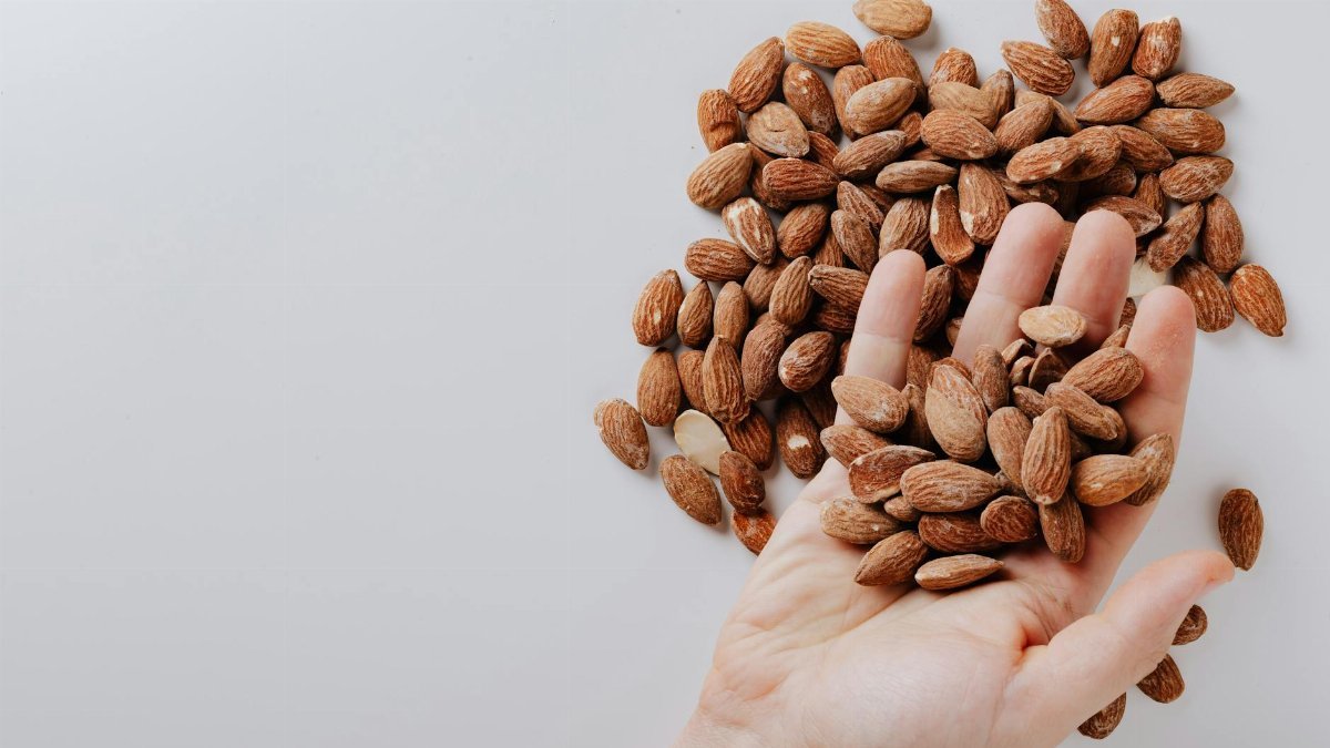 From above of anonymous male taking tasty organic almonds from pile of nuts placed on white background isolated illustrating healthy food concept