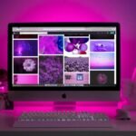 Modern desk setup with neon lighting and a desktop computer displaying colorful images.