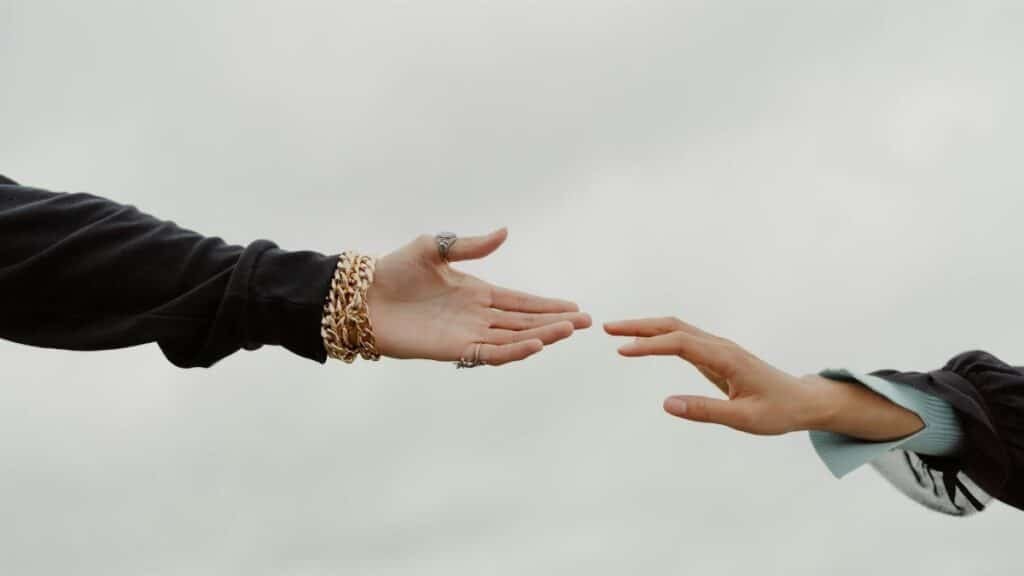Close-up of two hands reaching for each other under a cloudy sky, symbolizing connection.
