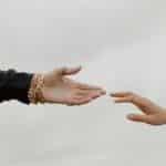 Close-up of two hands reaching for each other under a cloudy sky, symbolizing connection.