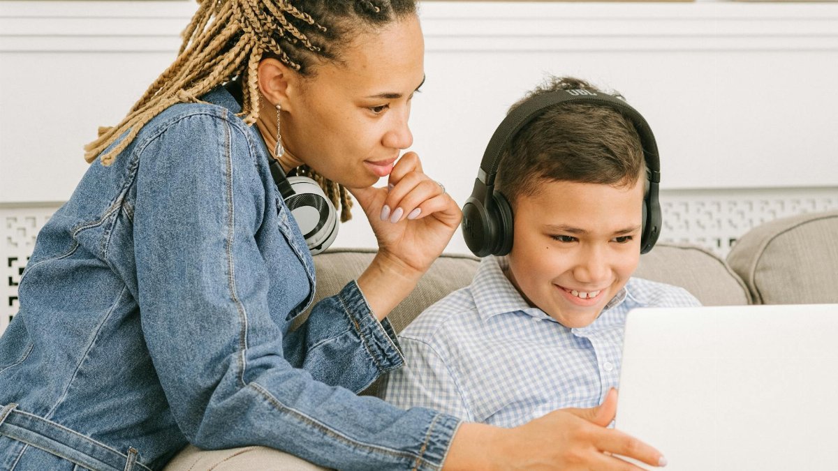 A mother and her son share a joyful online learning experience at home, smiling and engaged.