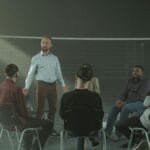 A diverse group participating in a therapy session with a facilitator indoors.