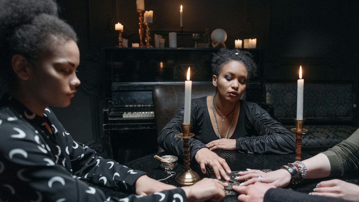 A group of women engaged in a seance around a candlelit ouija board.