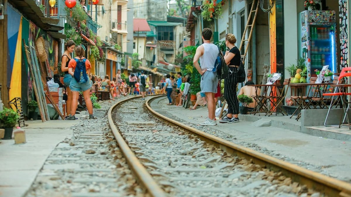 People relaxing at street cafes alongside railway tracks during daytime.