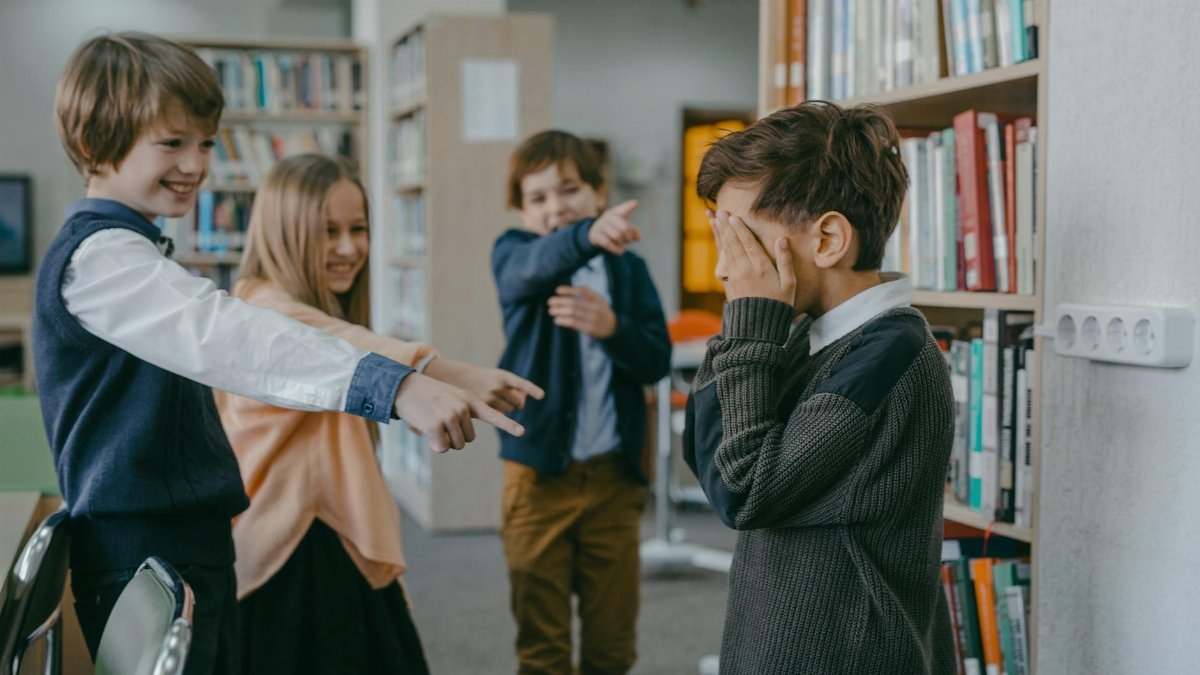Group of children bullying a classmate in a school library setting.