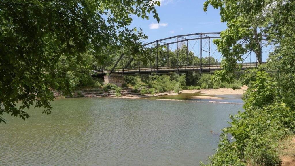 A picturesque view of War Eagle Bridge spanning a serene river surrounded by lush greenery in Arkansas.