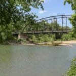 A picturesque view of War Eagle Bridge spanning a serene river surrounded by lush greenery in Arkansas.