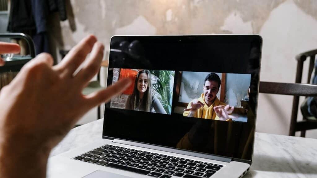Hands gesturing during a video call on a laptop screen, showing two people in a virtual meeting.