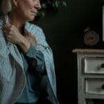 Senior woman sits by old TV, reflecting. Emotive indoor scene.