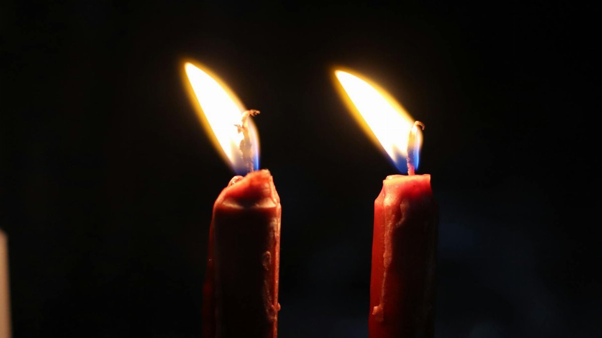 Warm glow of two lit candles casting light in darkness, symbolizing peace and spirituality.