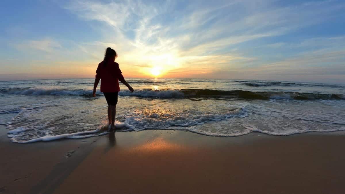 Woman walking along the beach at sunset, creating a serene and peaceful atmosphere.