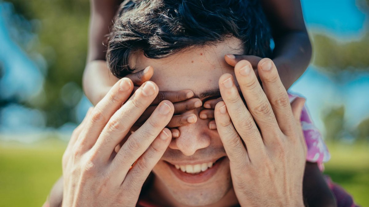 A child covers an adult's eyes in a playful outdoor game. Captures joy and connection.