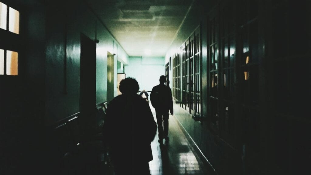 Silhouettes of people walking through a dimly lit corridor, creating an eerie atmosphere.