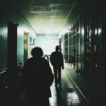 Silhouettes of people walking through a dimly lit corridor, creating an eerie atmosphere.