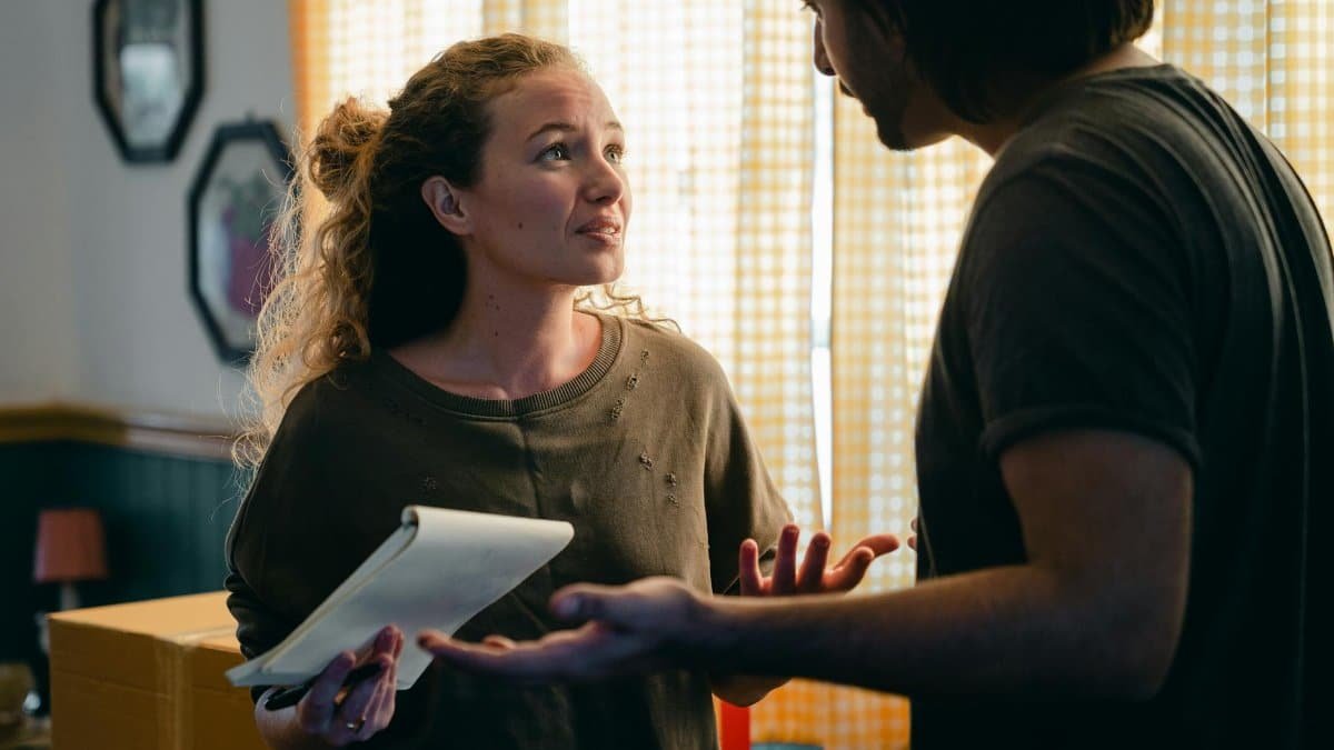 A couple talking in their living room surrounded by moving boxes, planning their new home setup.