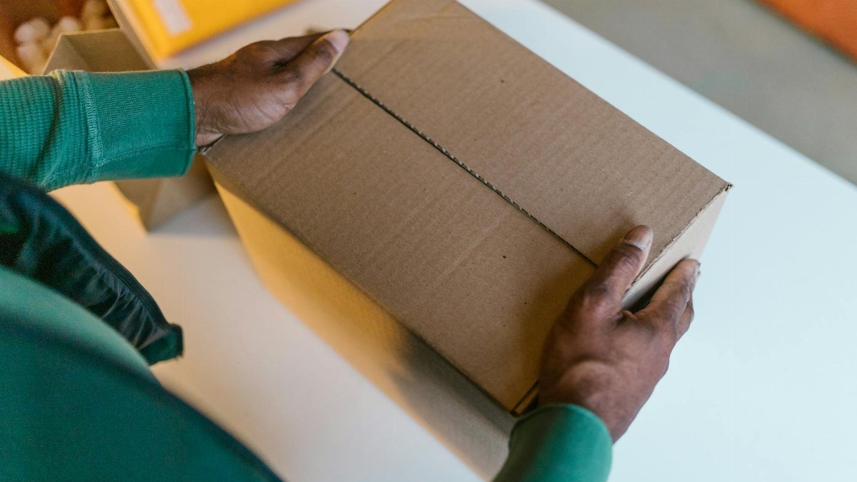 Close-up of hands holding a brown cardboard box on a white table indoors.