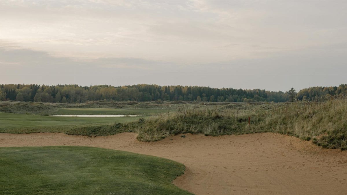 Peaceful landscape of a golf course with sand trap and distant forest at dawn.