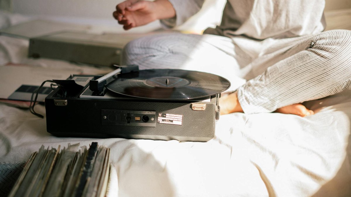 Relaxing morning scene with a close-up of a vintage record player and a person sitting on a bed in pajamas.