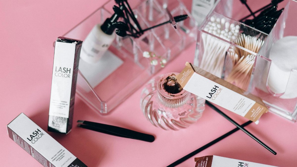 Flat lay of various cosmetic tools and products on a pink surface with clear organizers.