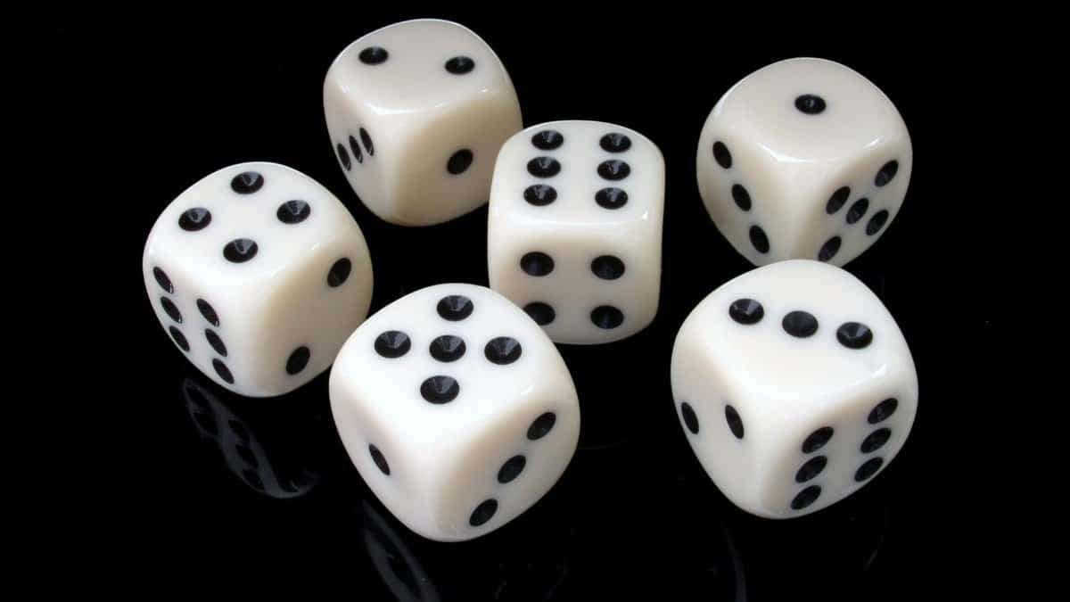 Set of white dice with black pips on a reflective black surface, showing various numbers.