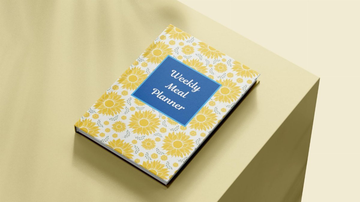 Weekly meal planner book with a floral cover on a minimalist surface, viewed from above.
