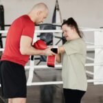 Boxing trainer helping young woman with Down syndrome during a training session in a gym.