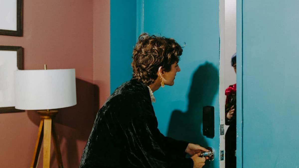 A person at a blue door surprised by a visitor holding flowers indoors.