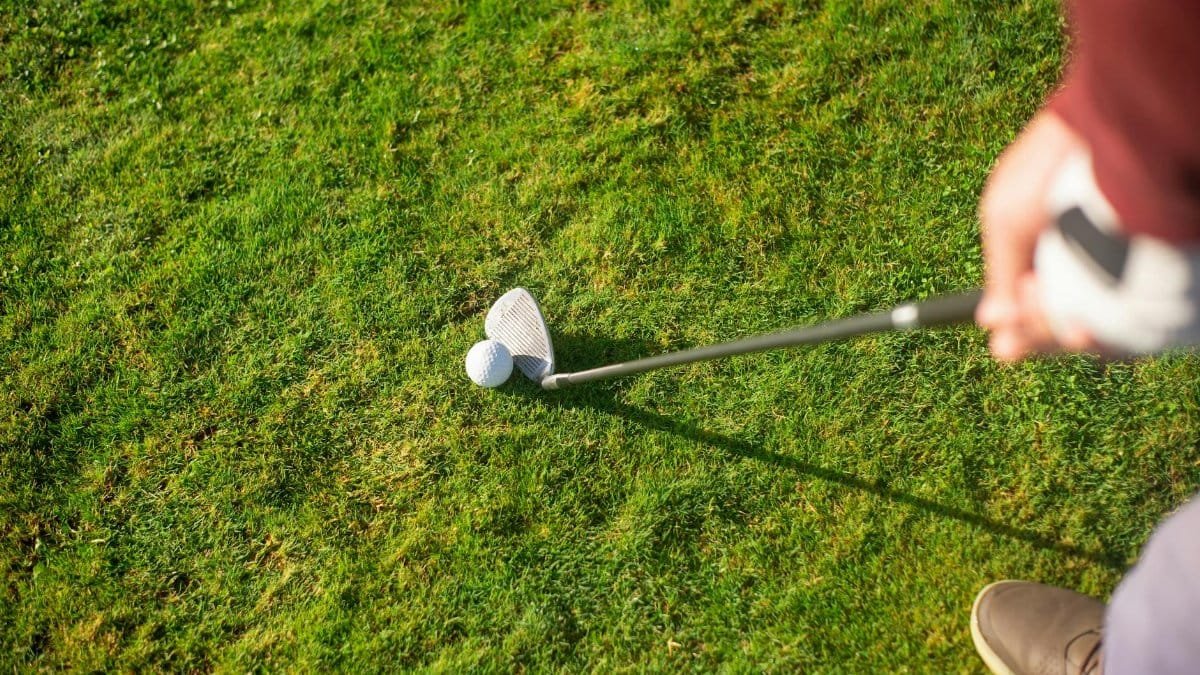 Close-up view of a golfer ready to swing with a club on a lush green grass field.
