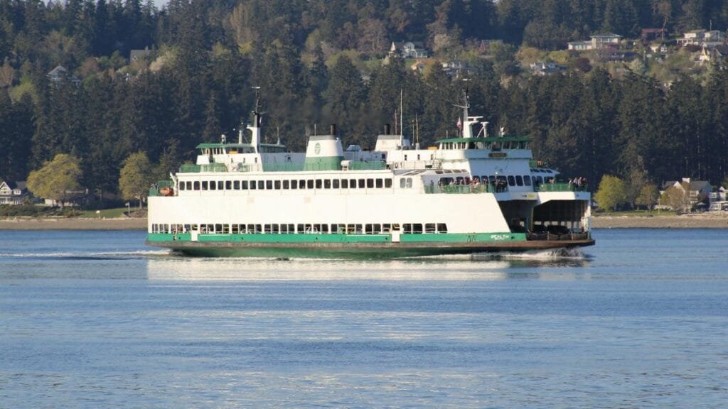 A Washington State Ferry sailing on the calm waters near Port Orchard, with a forested landscape in the background.